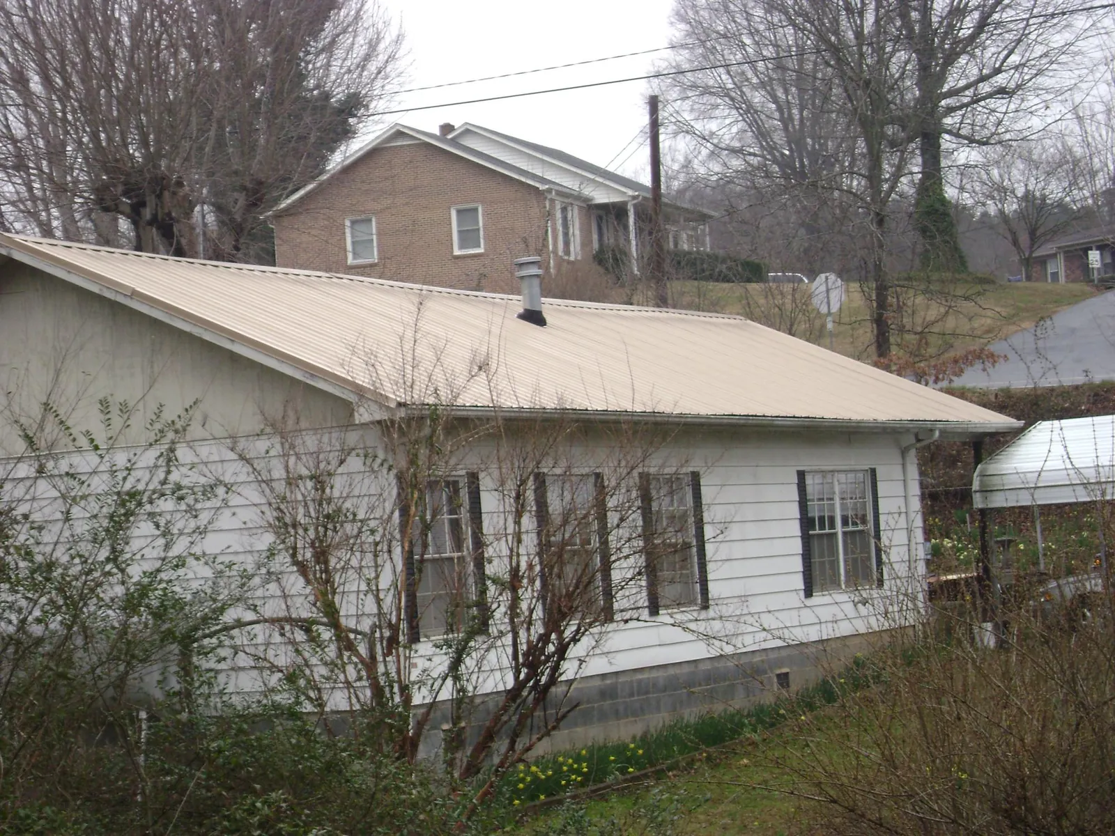 Tan metal roof on a white sided house set into a hillside — Commercial Roofing by Roofing Brothers in Miami Gardens