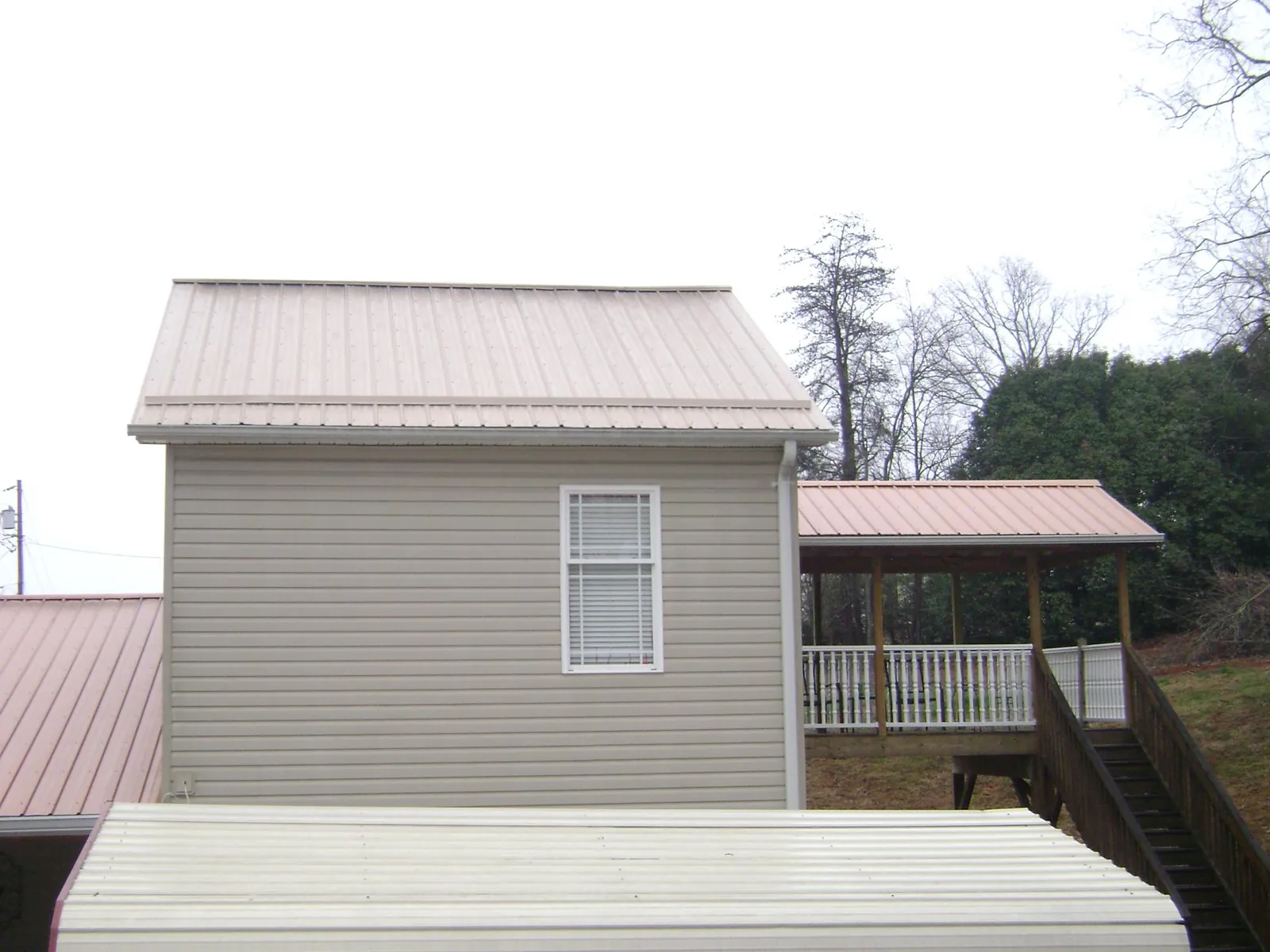 Tan metal roofs on a two story addition and attached porch, from a Roof Replacement job in Miami Gardens